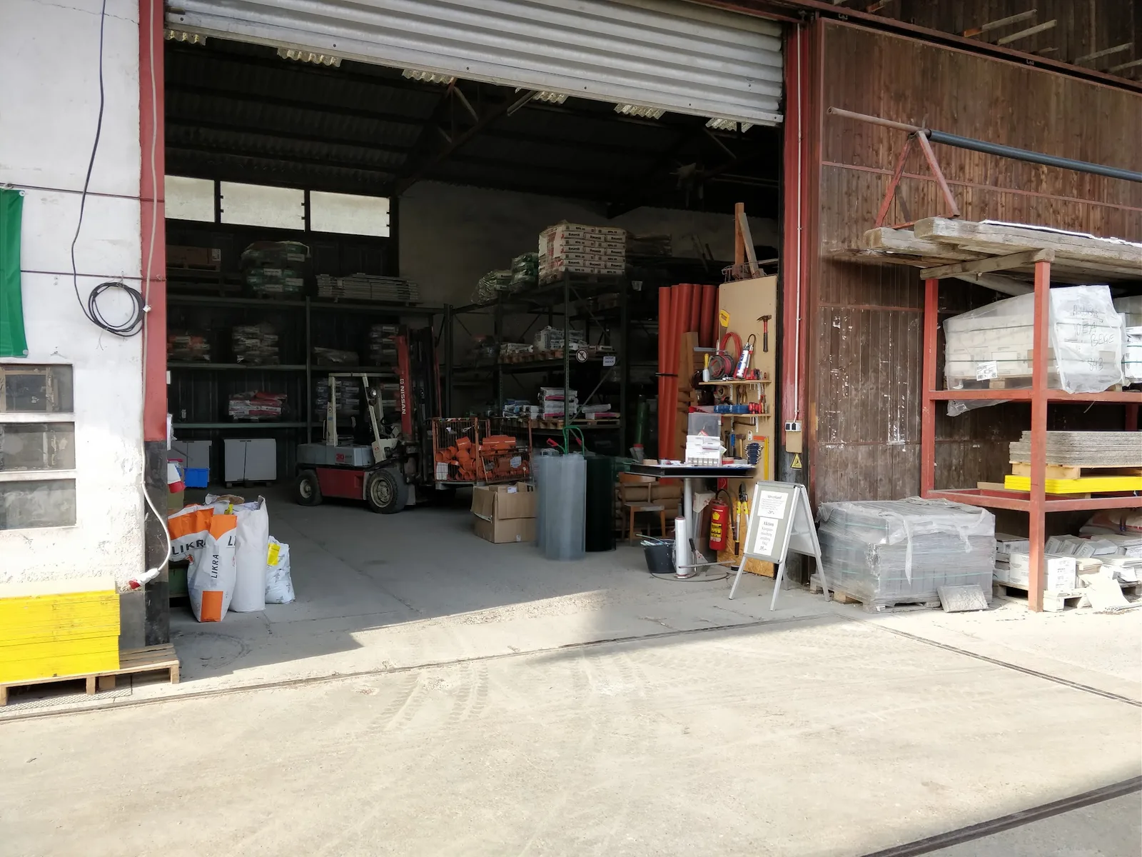 Offene Lagerhalle mit Regalen, Baustoffen, Werkzeugwand und Gabelstapler