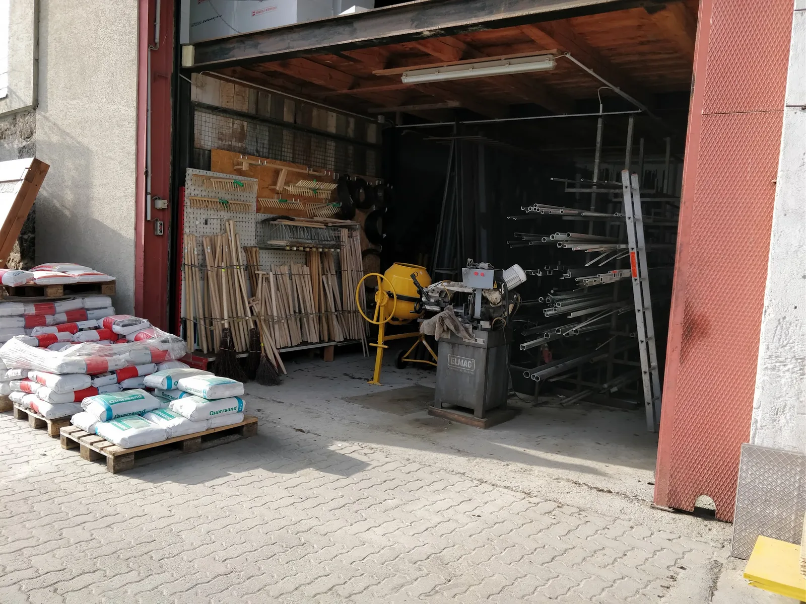 Lagerhalle mit Werkzeugstielen, Betonmischer, Metallsäge, Rohren und Quarzsand